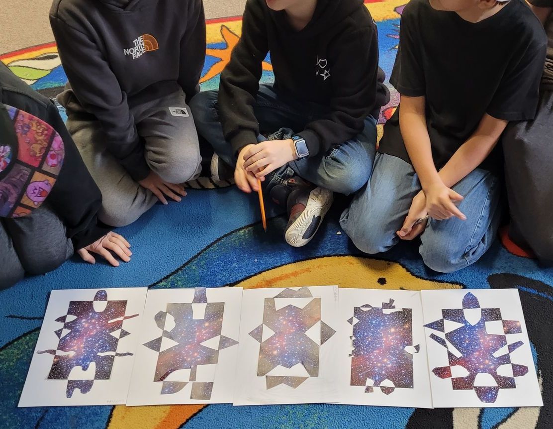 A group of children are sitting on the floor looking at a piece of paper with a galaxy on it