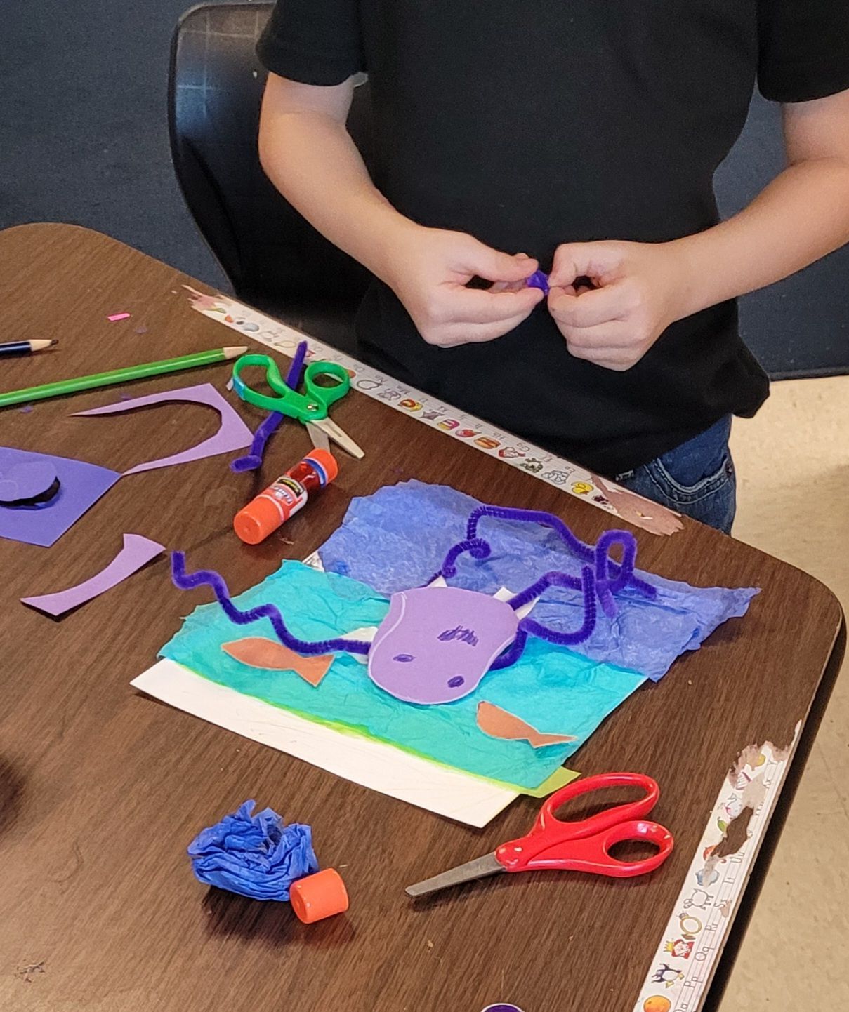 A child is sitting at a table with scissors and glue