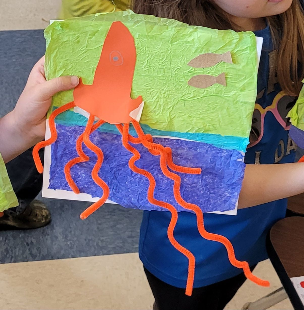 A girl in a blue shirt is holding a painting of an octopus