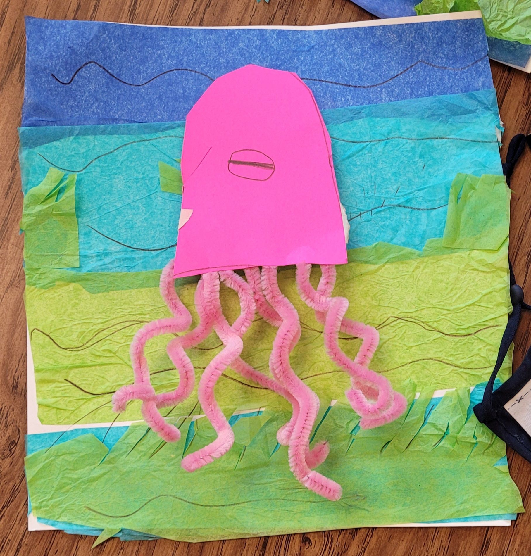 A pink octopus made out of pipe cleaners on a piece of paper