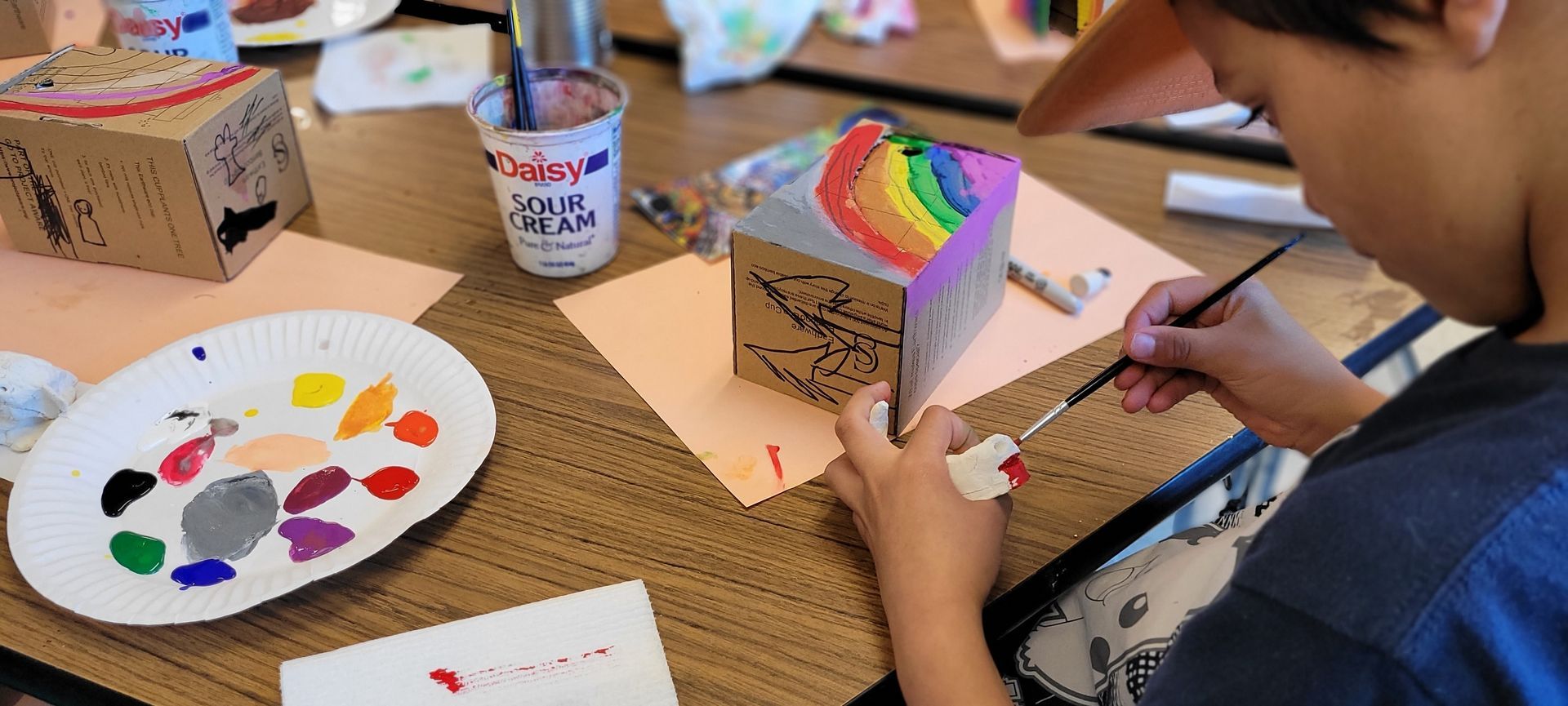 A young boy is painting a cardboard box with a brush.
