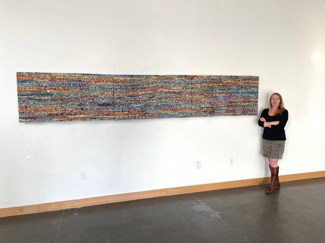 A woman is standing in front of a large MOSAIC on a wall.