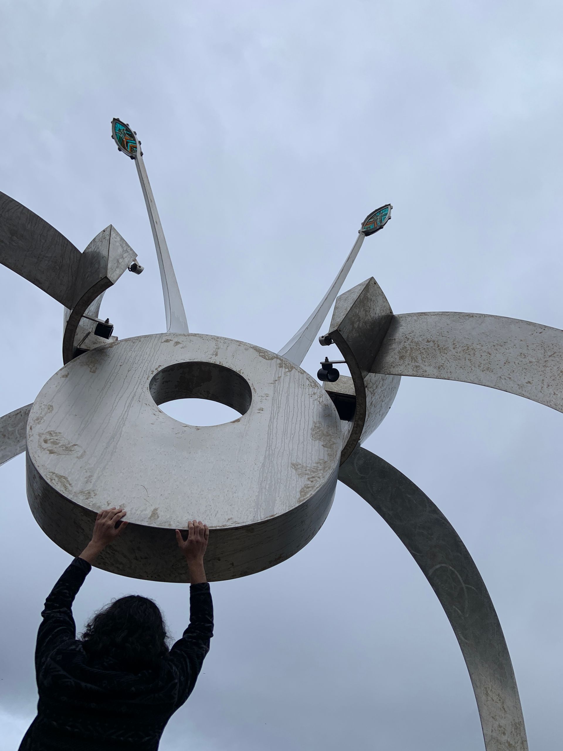 A person is reaching up to a large metal sculpture