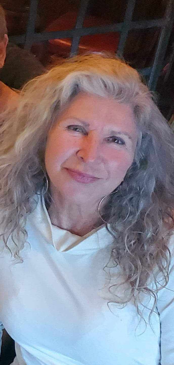 A woman with curly hair is wearing a white shirt and smiling for the camera.