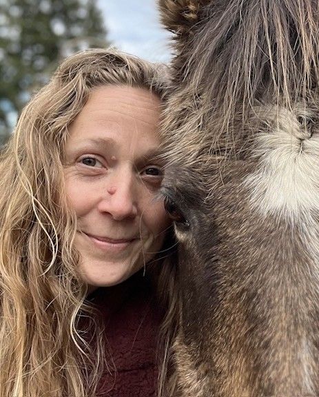A woman is standing next to a horse and smiling.