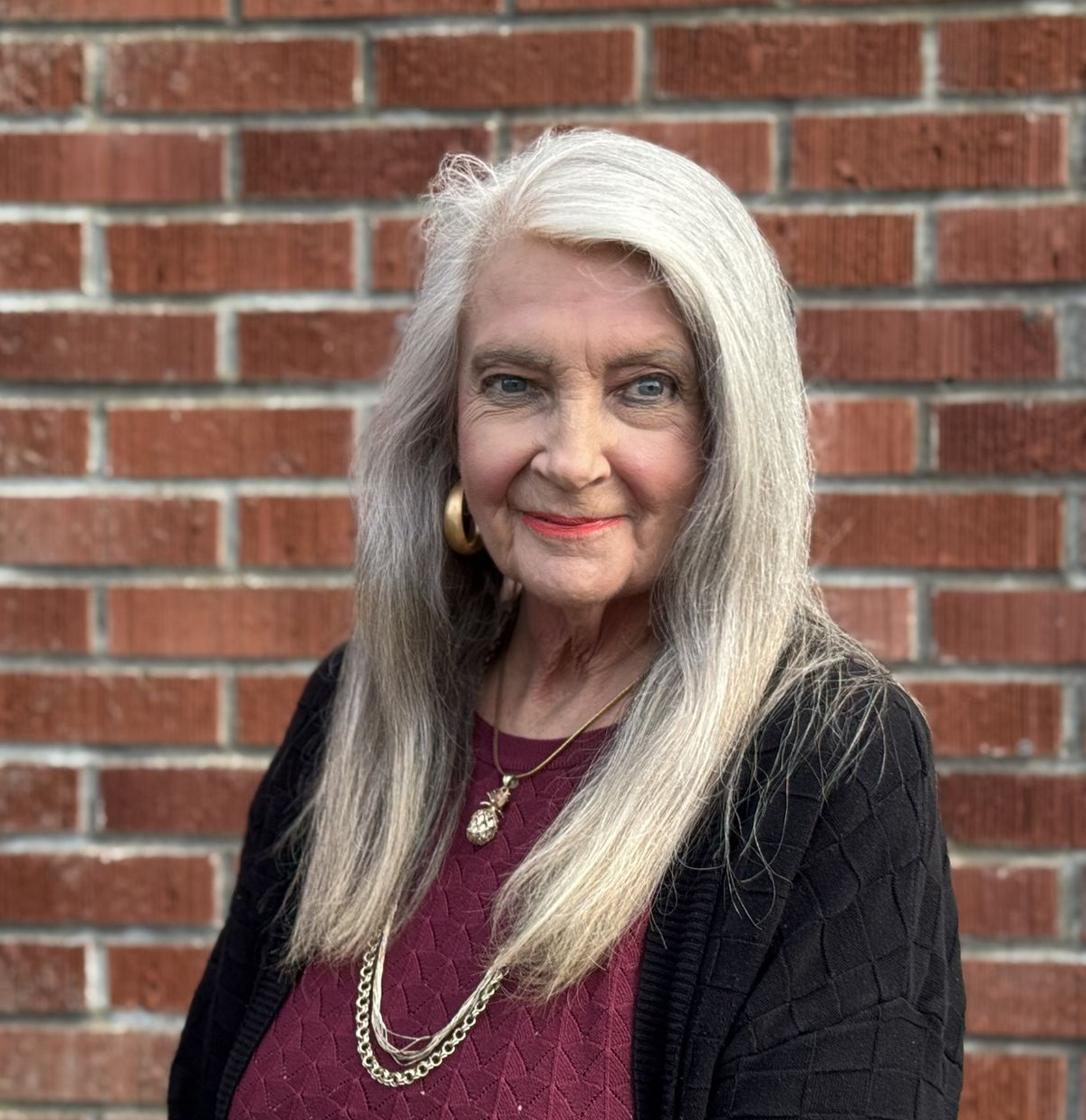 A woman wearing a blue jacket and a gold necklace is smiling.