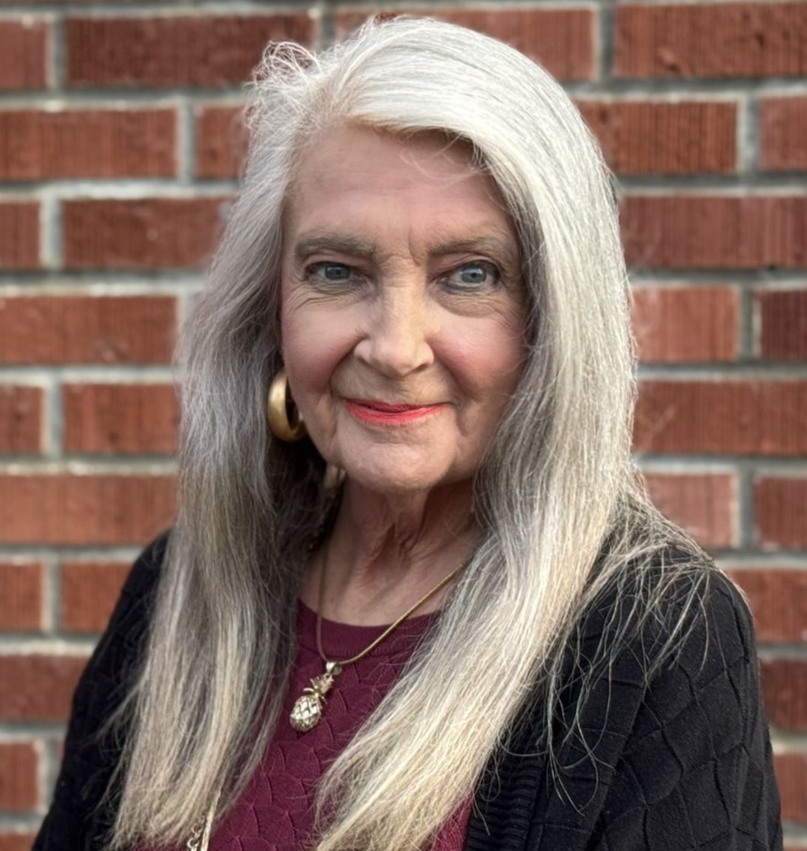 A woman wearing a blue jacket and a gold necklace is smiling.