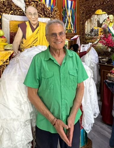 A man in a green shirt is standing in front of a statue of a monk.