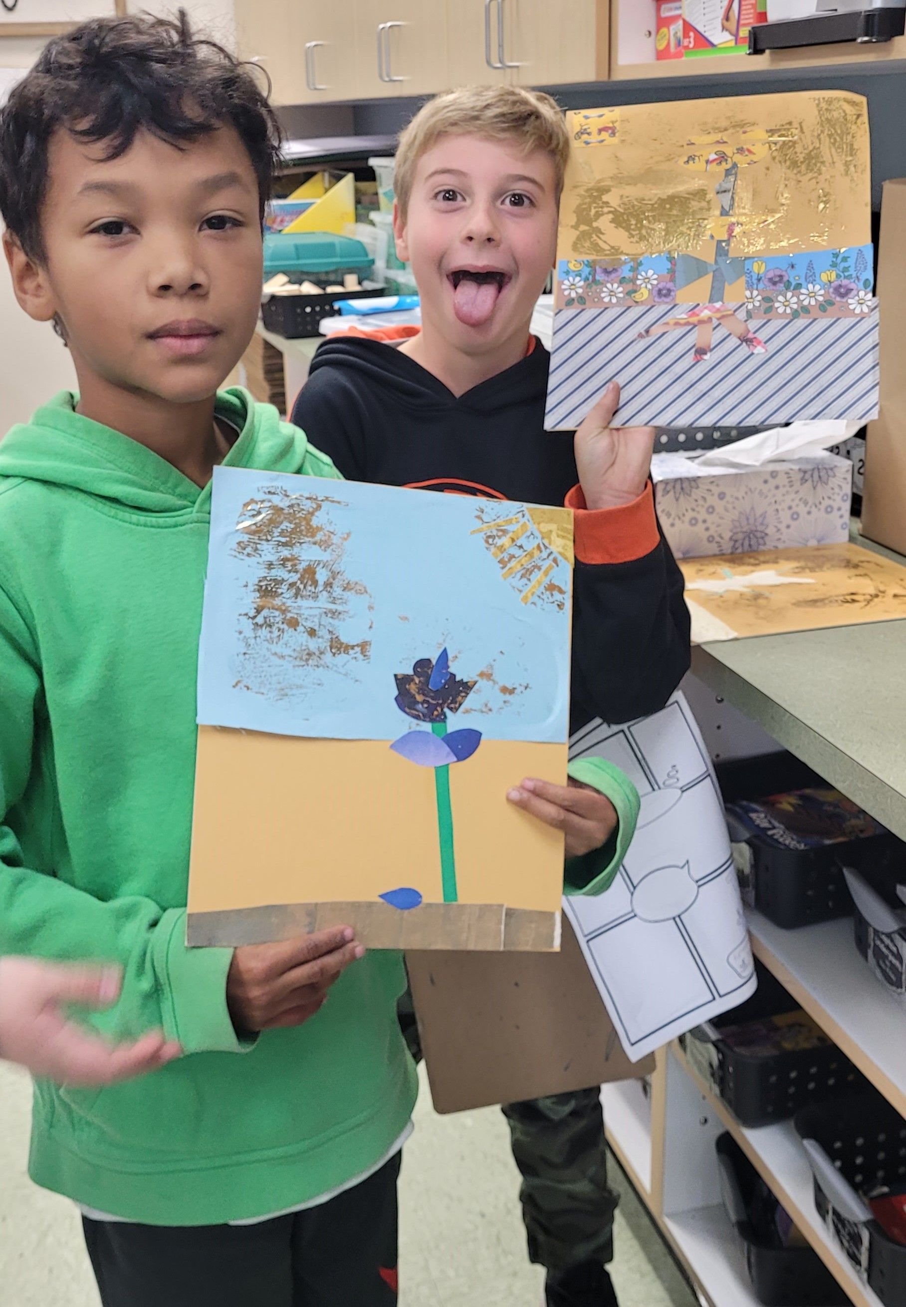 Two young boys are holding up their artwork in a classroom.