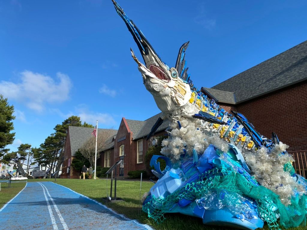 A statue of a marlin made out of plastic bottles is in front of a building.