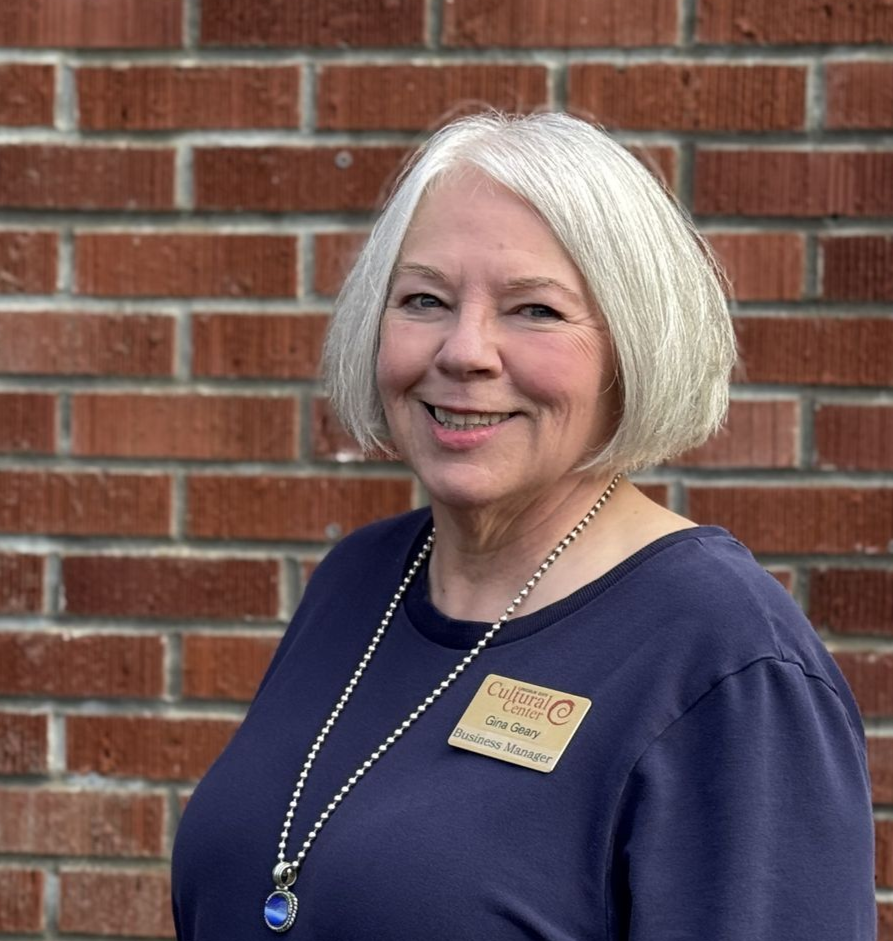 A woman with white hair is sitting at a table smiling.