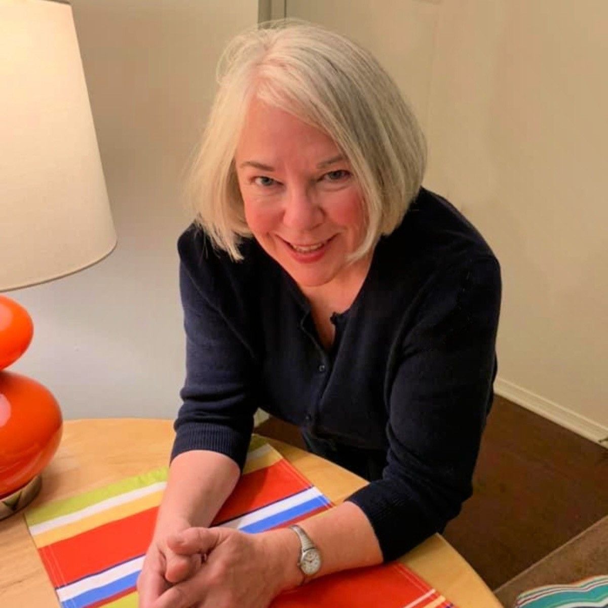 A woman with white hair is sitting at a table smiling.