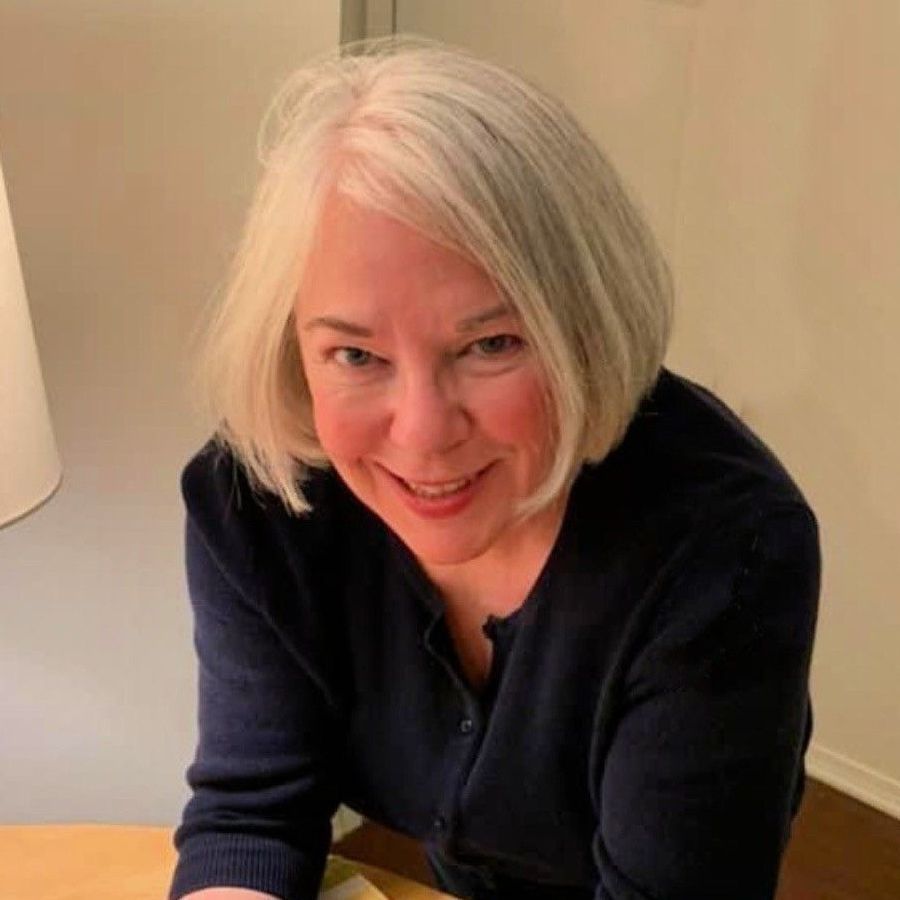 A woman with white hair is sitting at a table smiling.