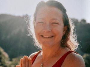 A woman in a red tank top is smiling and holding her hands together.