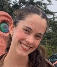 A young woman is smiling in front of a statue of an alien.