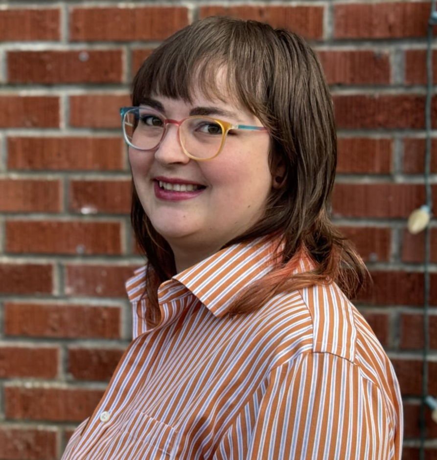 A woman wearing a black shirt with a flower pattern and a black blazer on is smiling.
