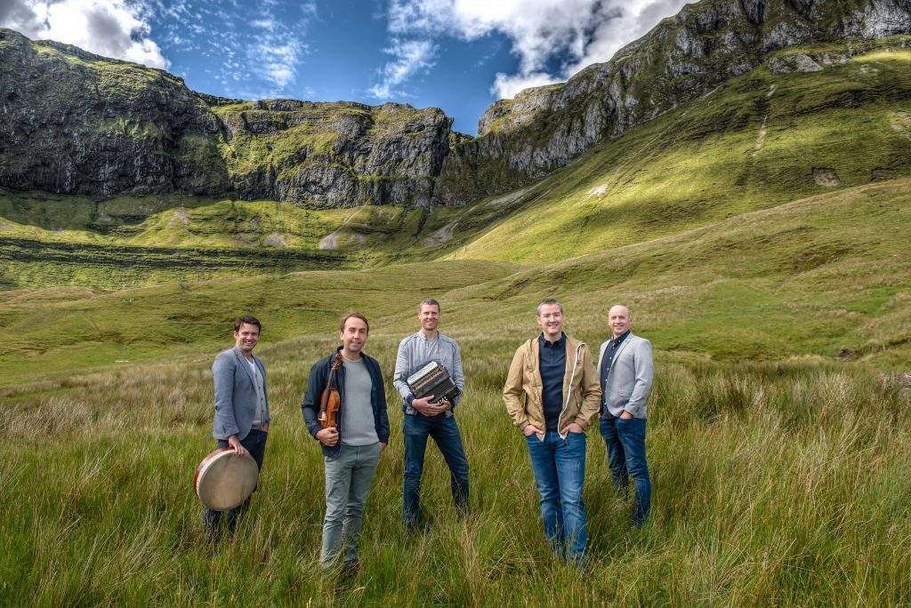 Members of the band Téada standing with instruments in a grassy meadow