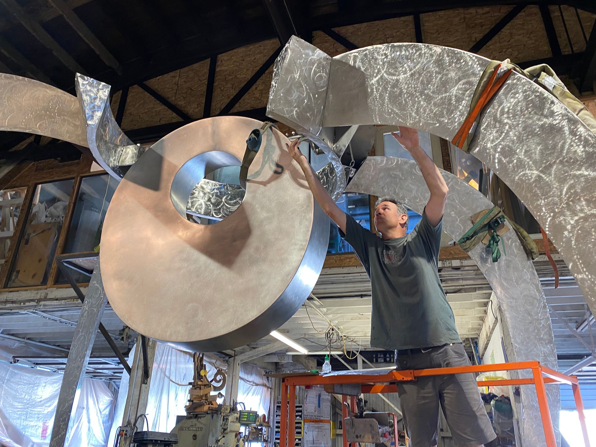 A man is working on a large metal sculpture in a workshop.