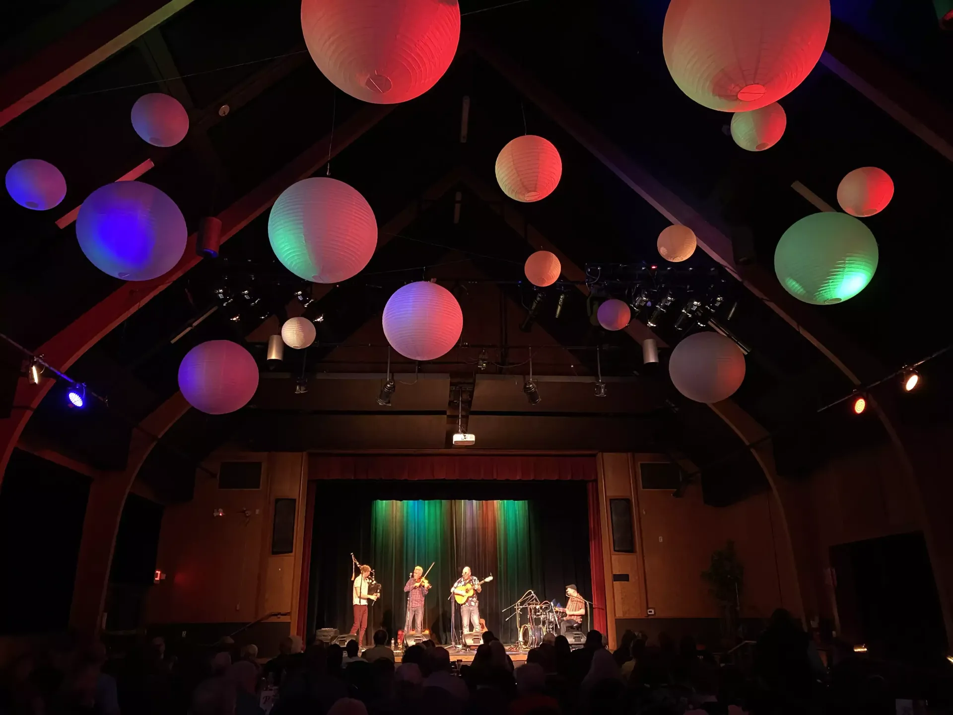 A group of people are playing instruments on a stage with lanterns hanging from the ceiling.