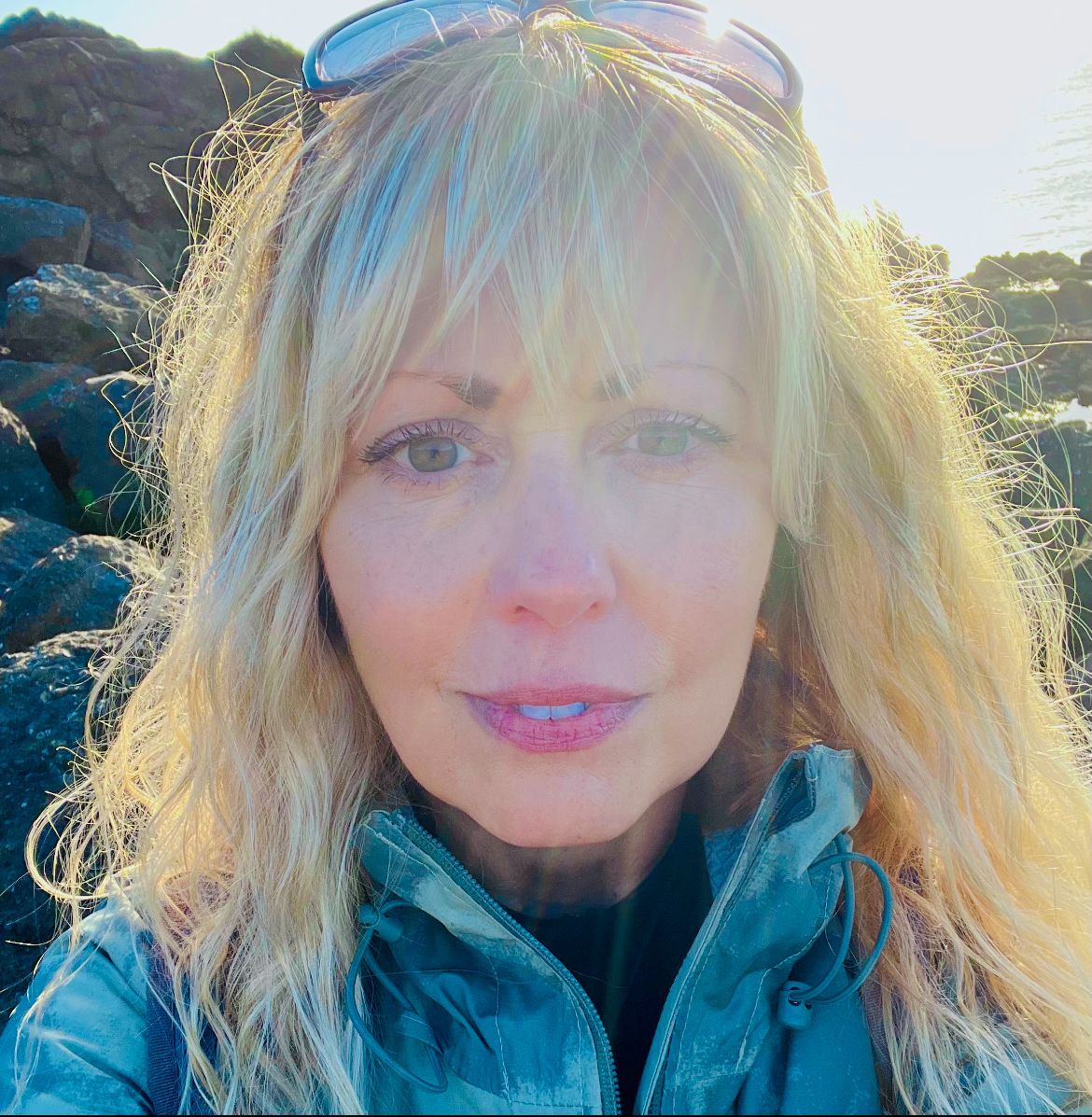 A woman wearing sunglasses and a jacket is taking a selfie.