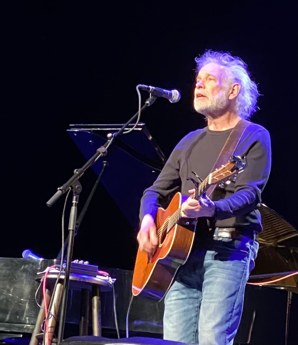 A man singing into a microphone while holding an acoustic guitar