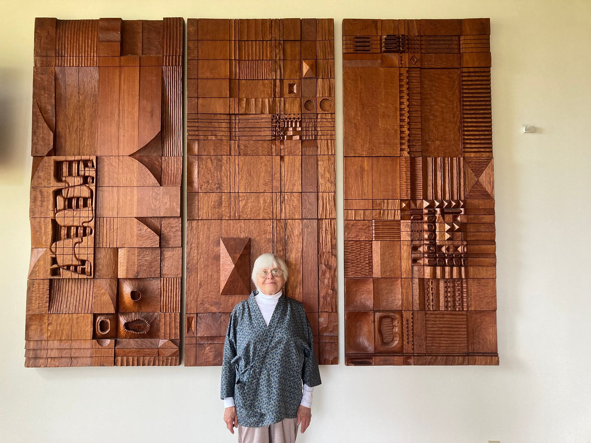 A woman is standing in front of a wood carving on a wall