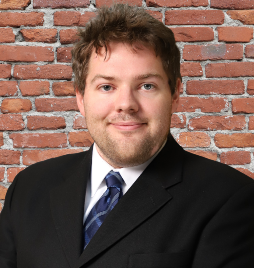 A woman wearing a black shirt with a flower pattern and a black blazer on is smiling.