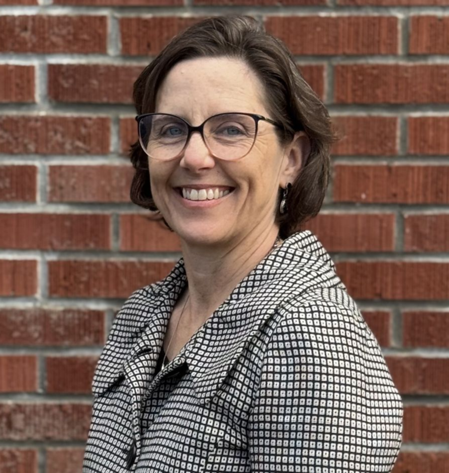 A woman with white hair is sitting at a table smiling.