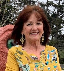 A woman in a yellow shirt and earrings is smiling for the camera.