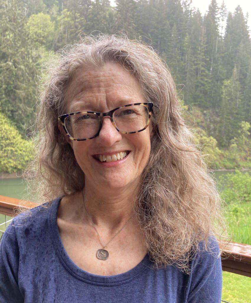 A woman wearing glasses and a blue shirt is smiling for the camera.