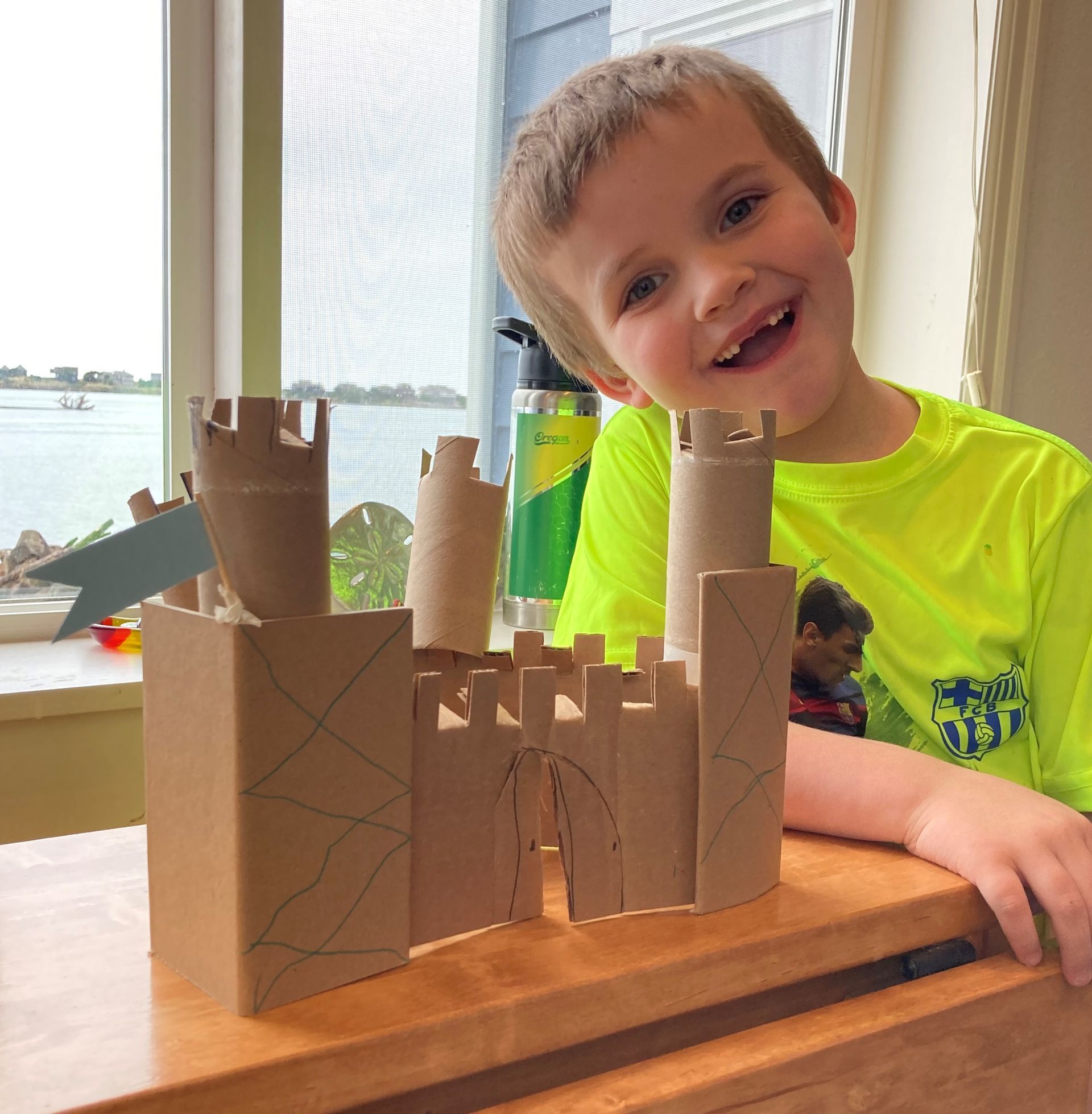 A young boy is sitting at a table with a cardboard castle made out of toilet paper rolls