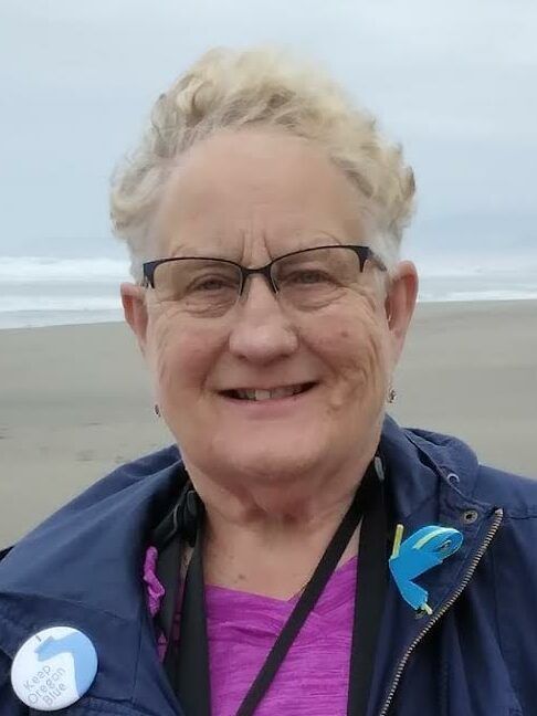 A woman wearing glasses and a purple shirt is smiling on the beach