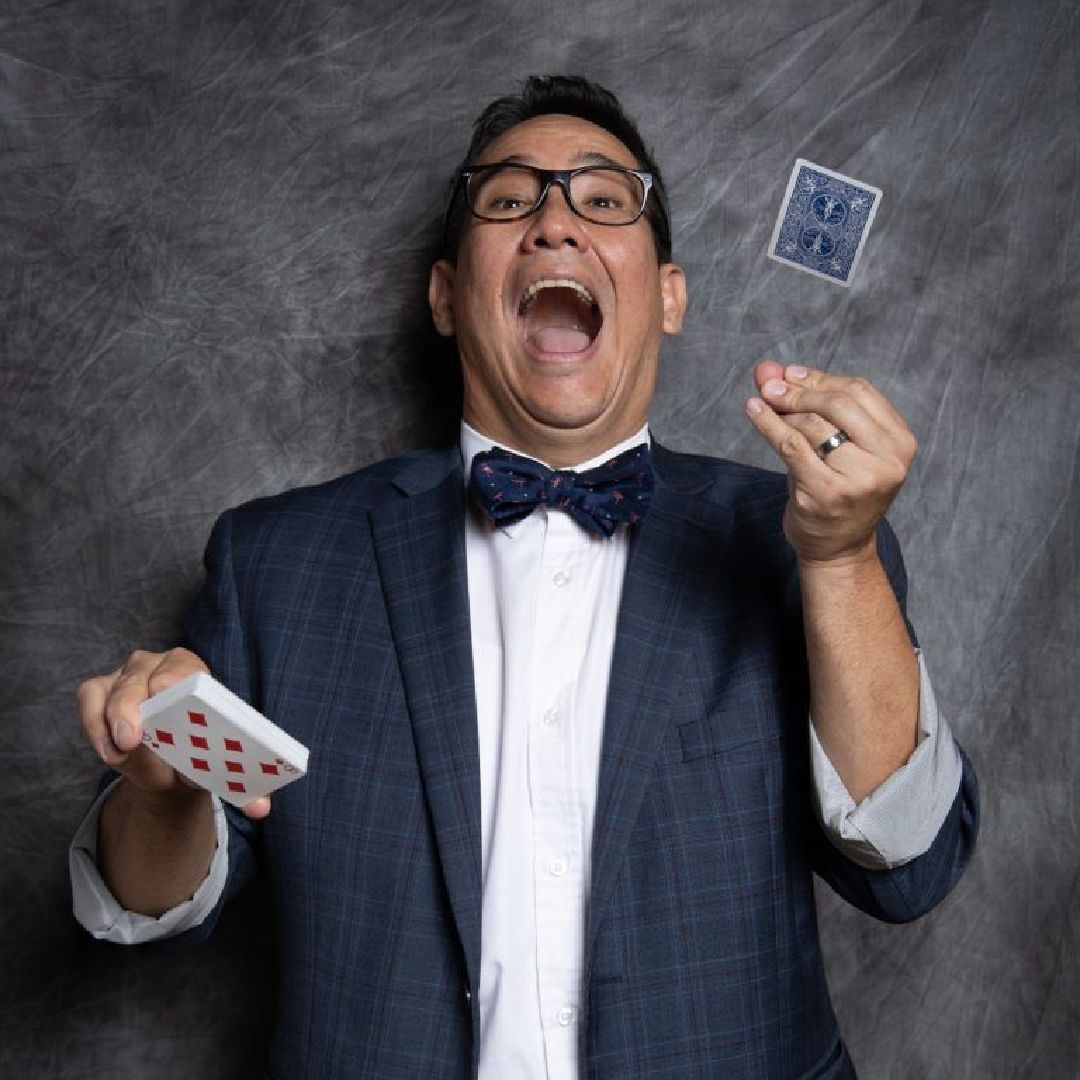A man in a suit and bow tie is throwing playing cards in the air FOI - Magic - Spring Break