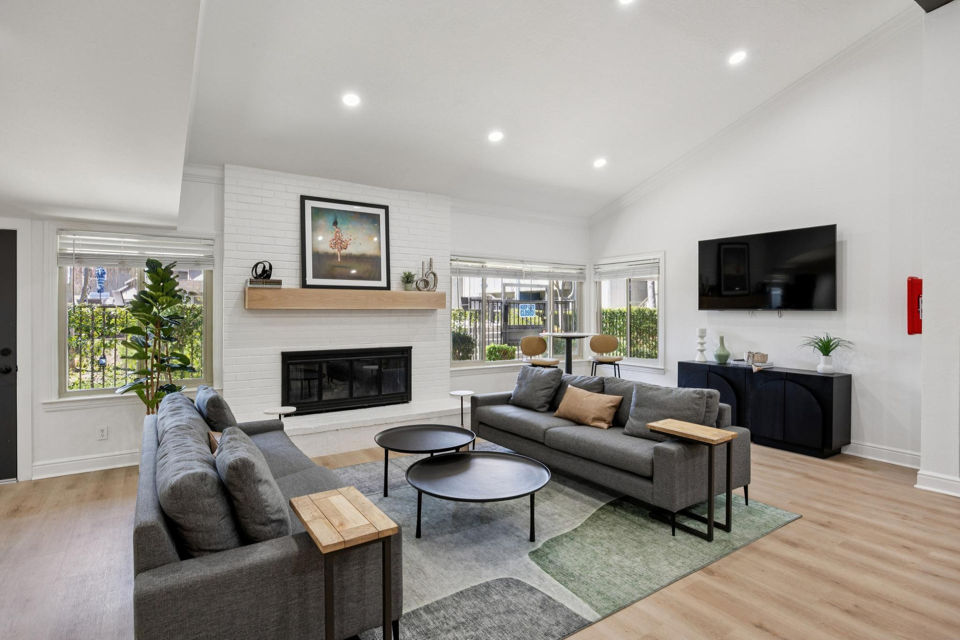 Spacious living room with gray sofas, fireplace, and mounted TV. Features light wood floors and large windows.
