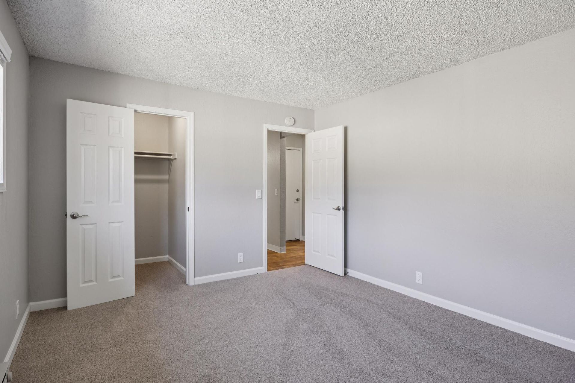 Empty bedroom with gray walls, carpet, two closets, and an open doorway.