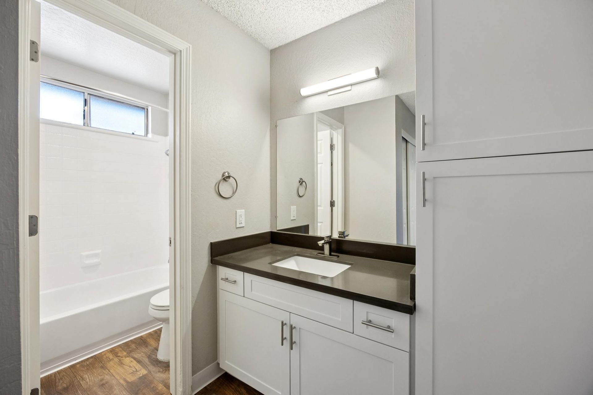 Bathroom with white cabinets, dark countertop, large mirror, and open doorway to a bathtub.