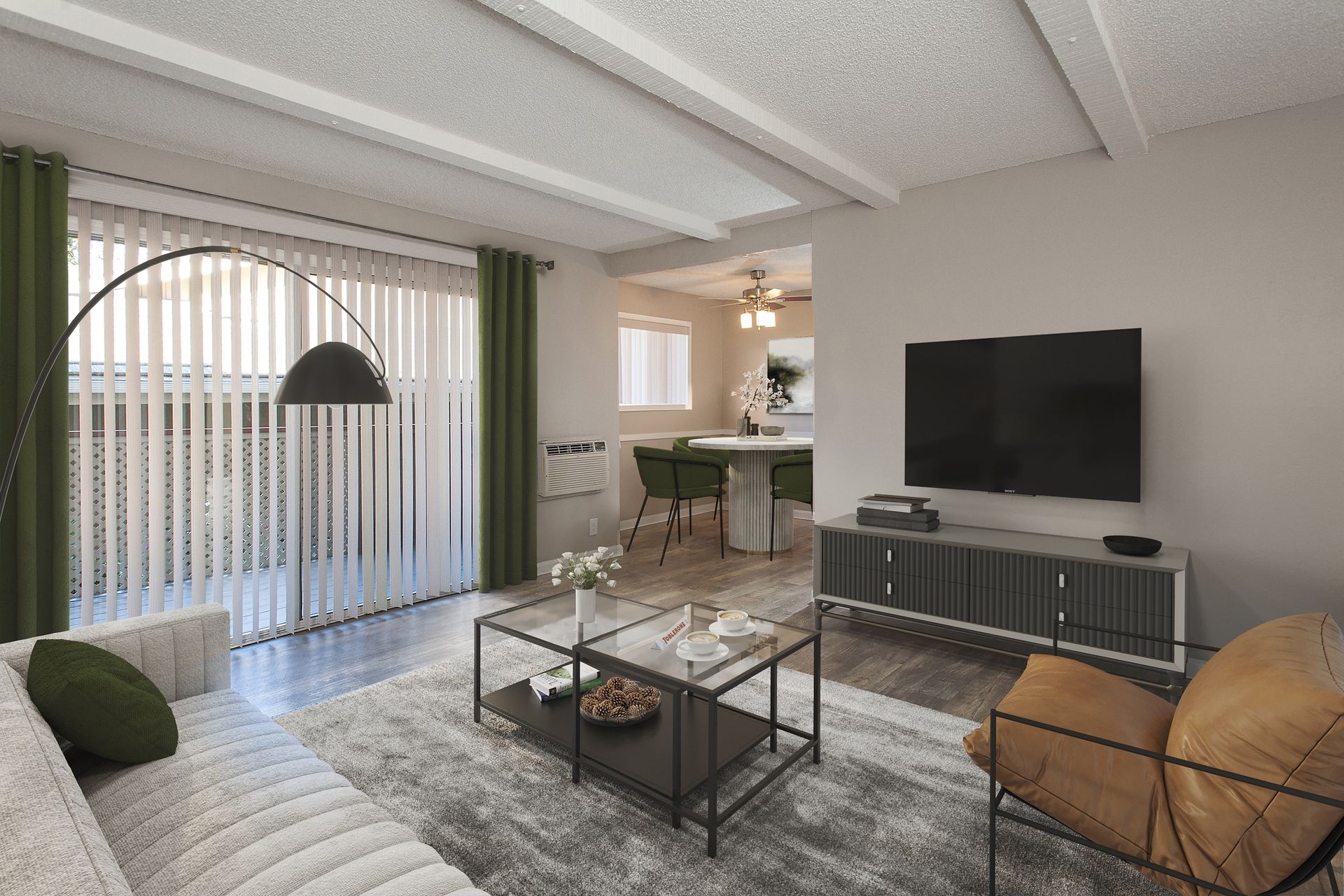 Living room with gray sofa, glass coffee table, TV on a console, open dining area in background.