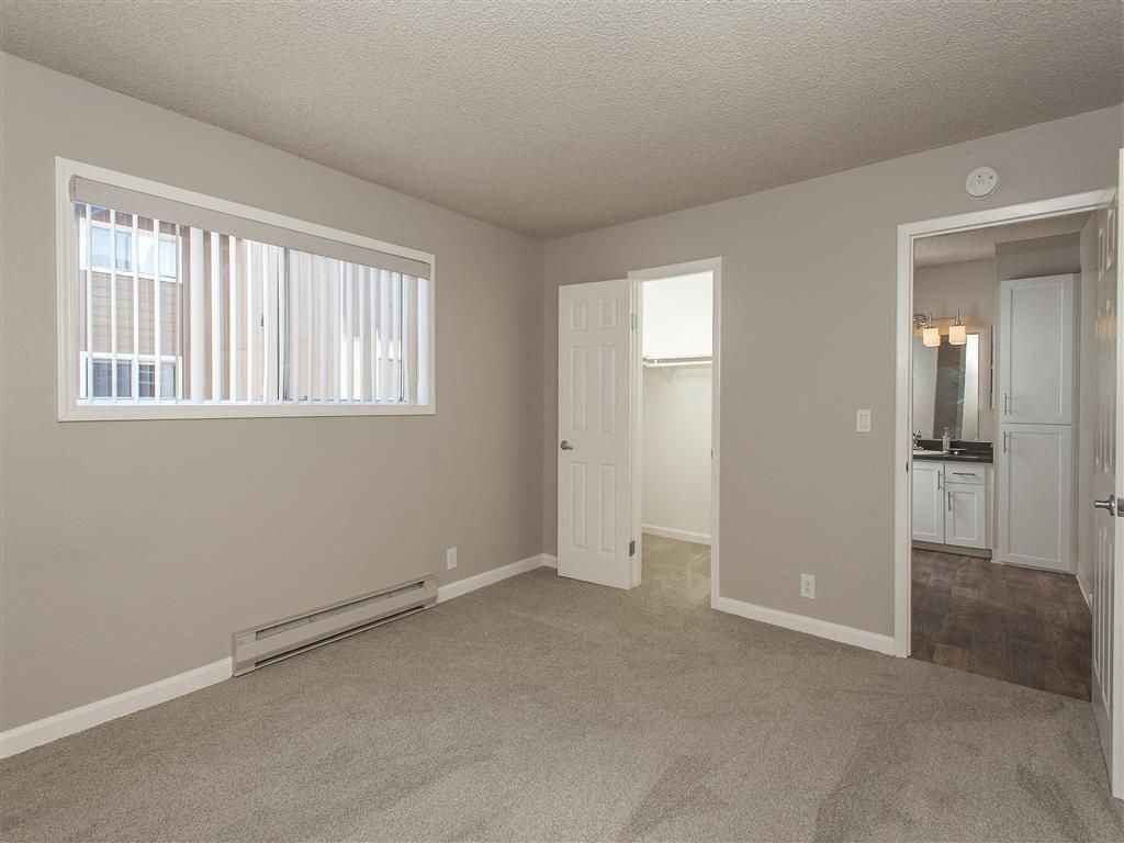 Neutral-toned apartment bedroom with a window, baseboard heater, and doorway to a bathroom.