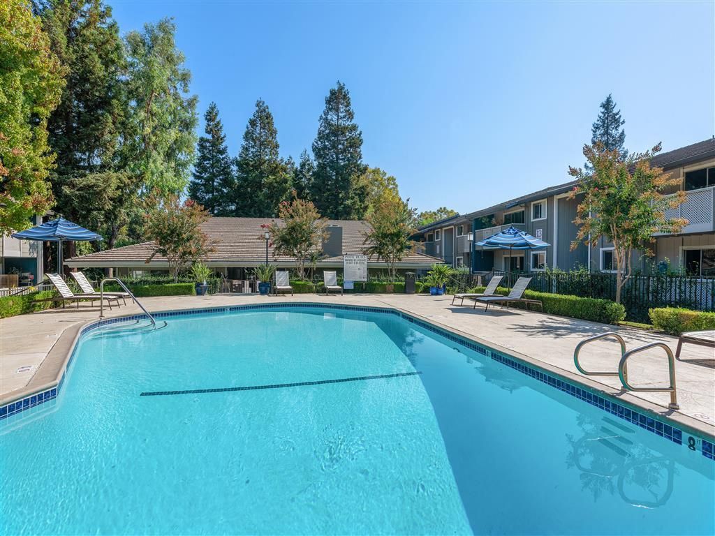 Outdoor pool area with lounge chairs and blue umbrellas at a residential complex.