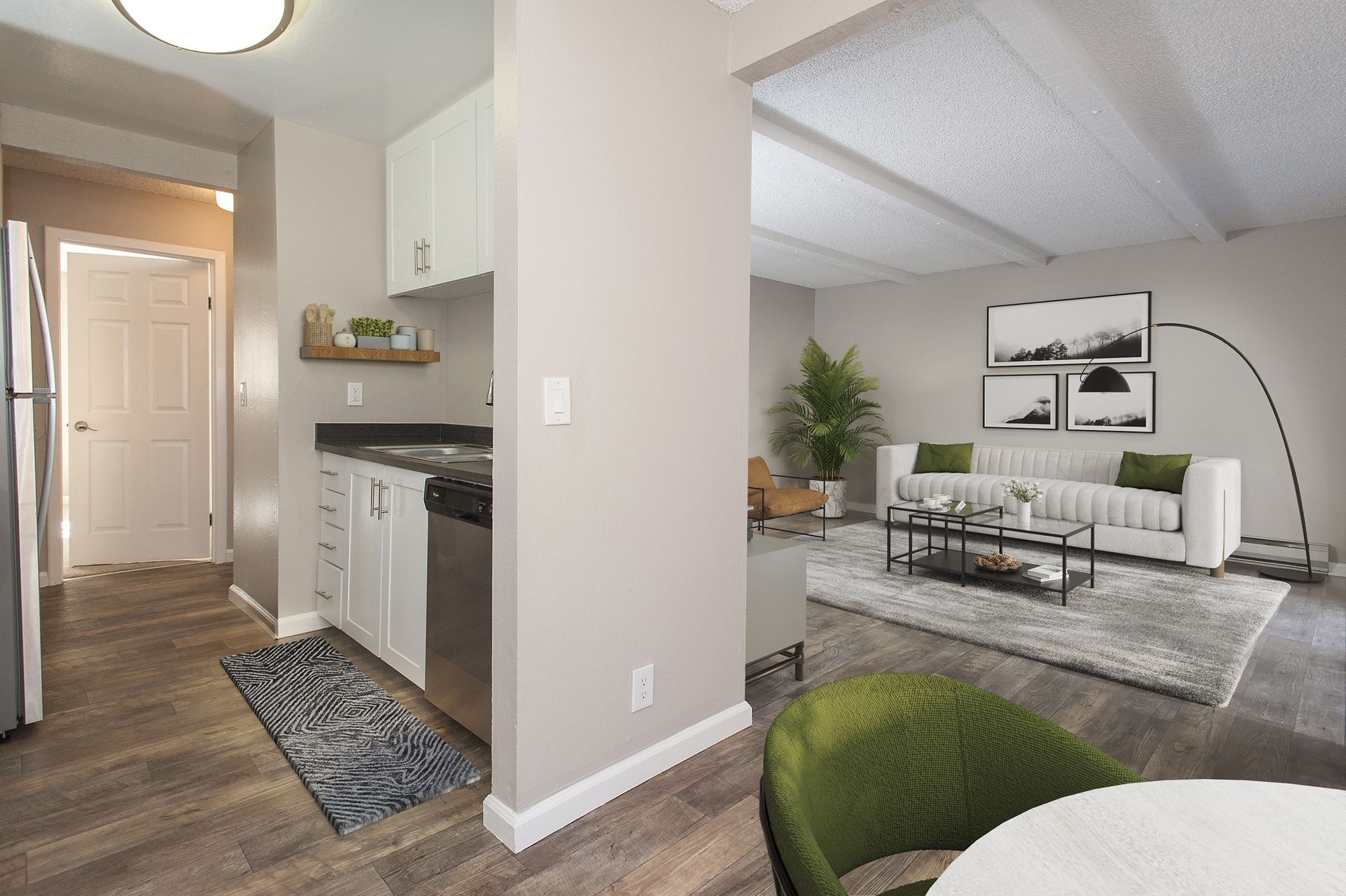 Open-concept apartment interior with a white kitchen on the left and a living area featuring a white sofa.