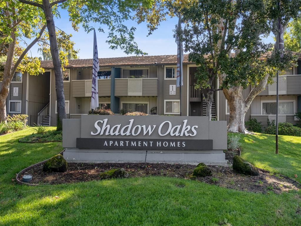 Exterior sign reading Shadow Oaks Apartment Homes in front of a multi-unit building.
