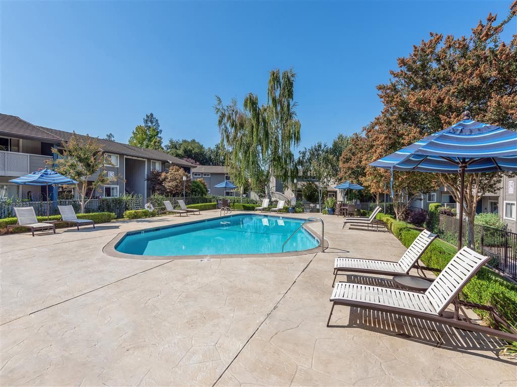 Outdoor apartment pool area with lounge chairs and blue umbrellas.