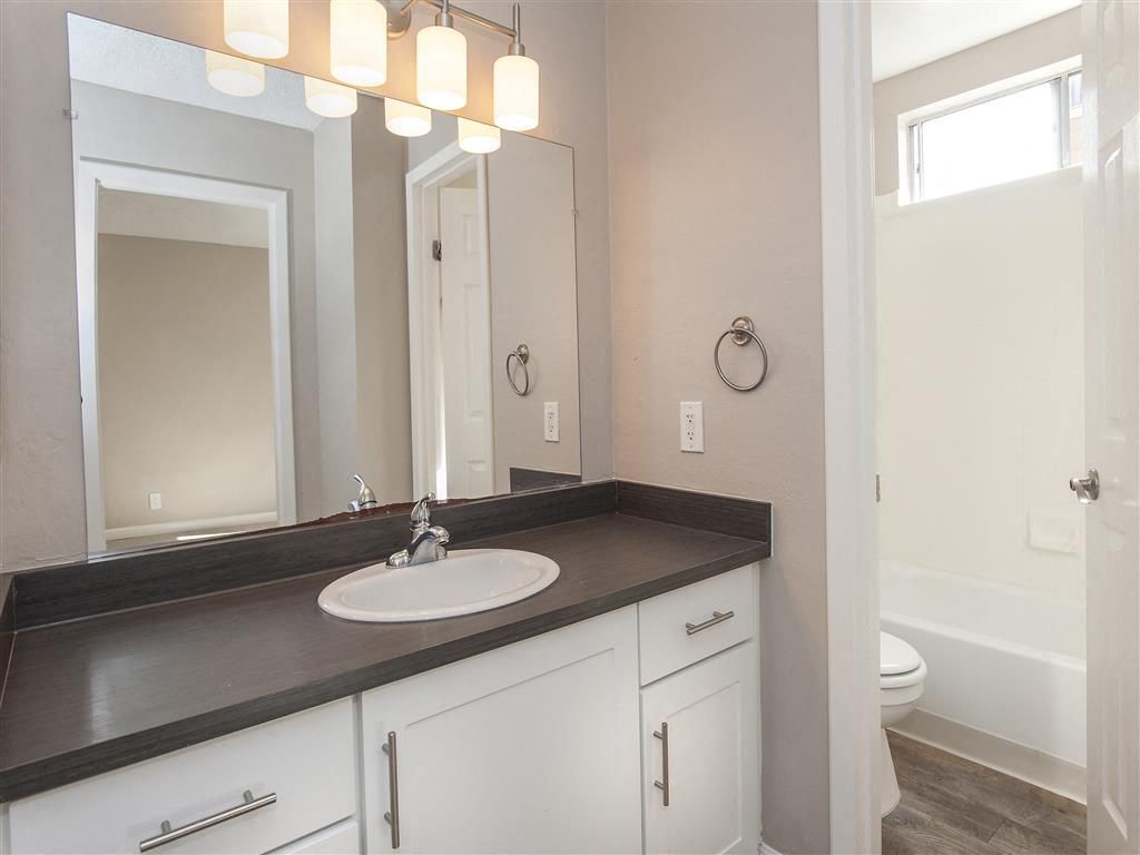 Bathroom vanity with dark countertop, white cabinetry, mirror, and tub/shower combo in an apartment.
