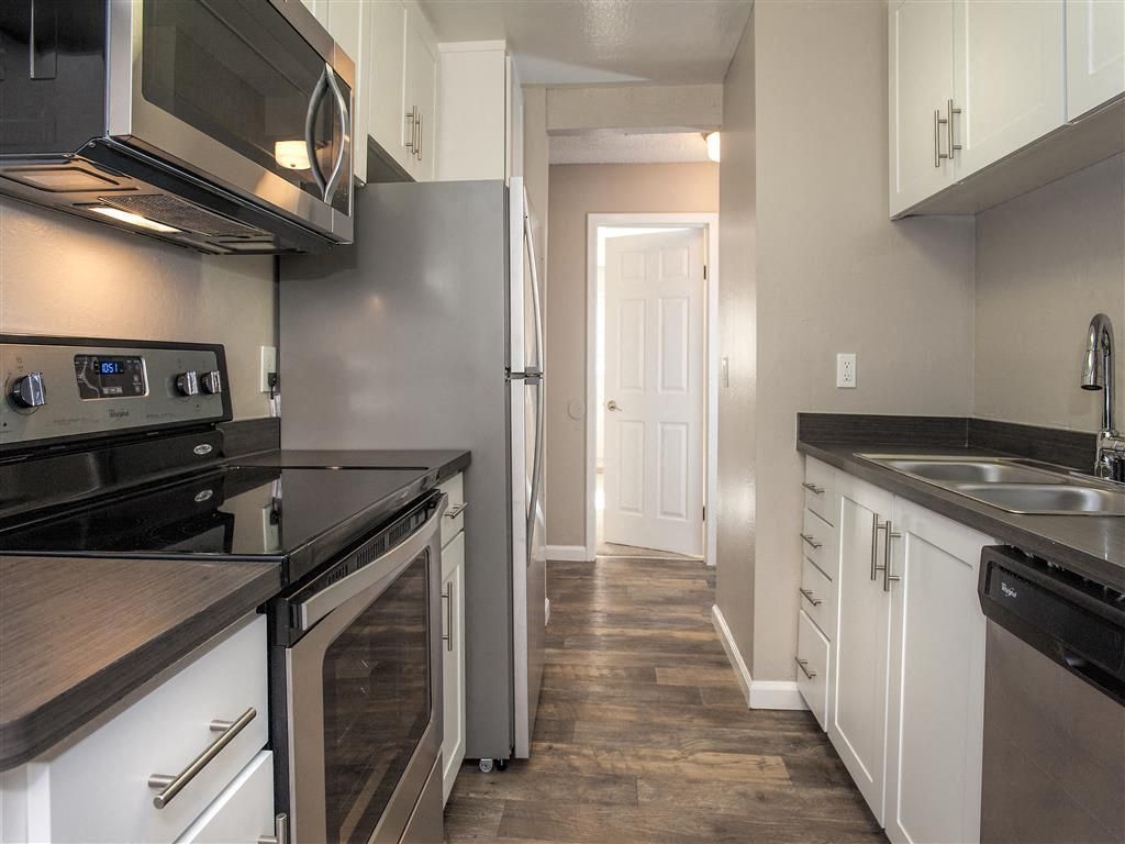 Galley kitchen with stainless steel appliances, white cabinets, and dark countertops.