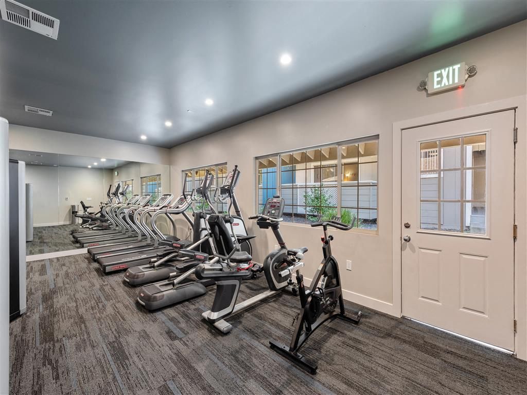 Indoor fitness center with treadmills and stationary bikes along a mirrored wall.