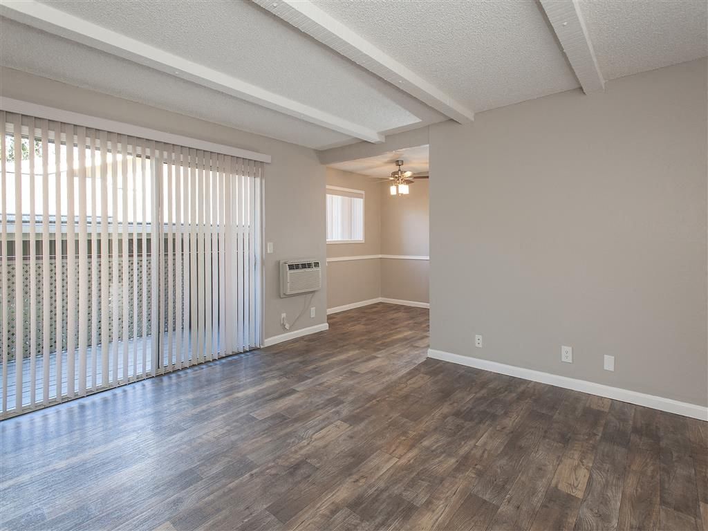 Living room with sliding glass door, vertical blinds, and wood-look flooring.