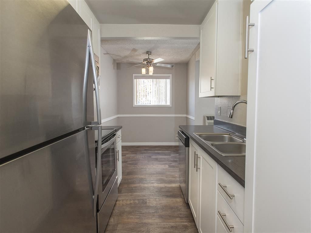 Galley-style kitchen with stainless steel appliances, white cabinets, and a window.