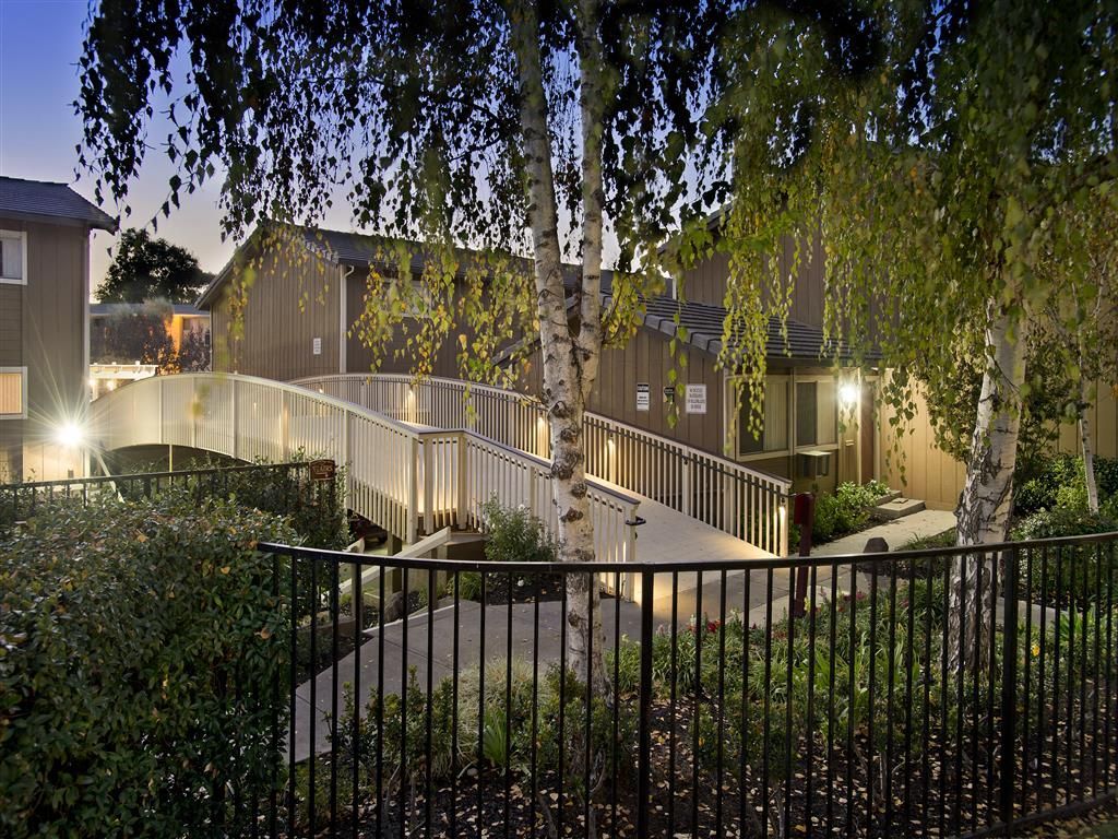 Exterior view of an apartment community with illuminated walkways and trees at dusk.