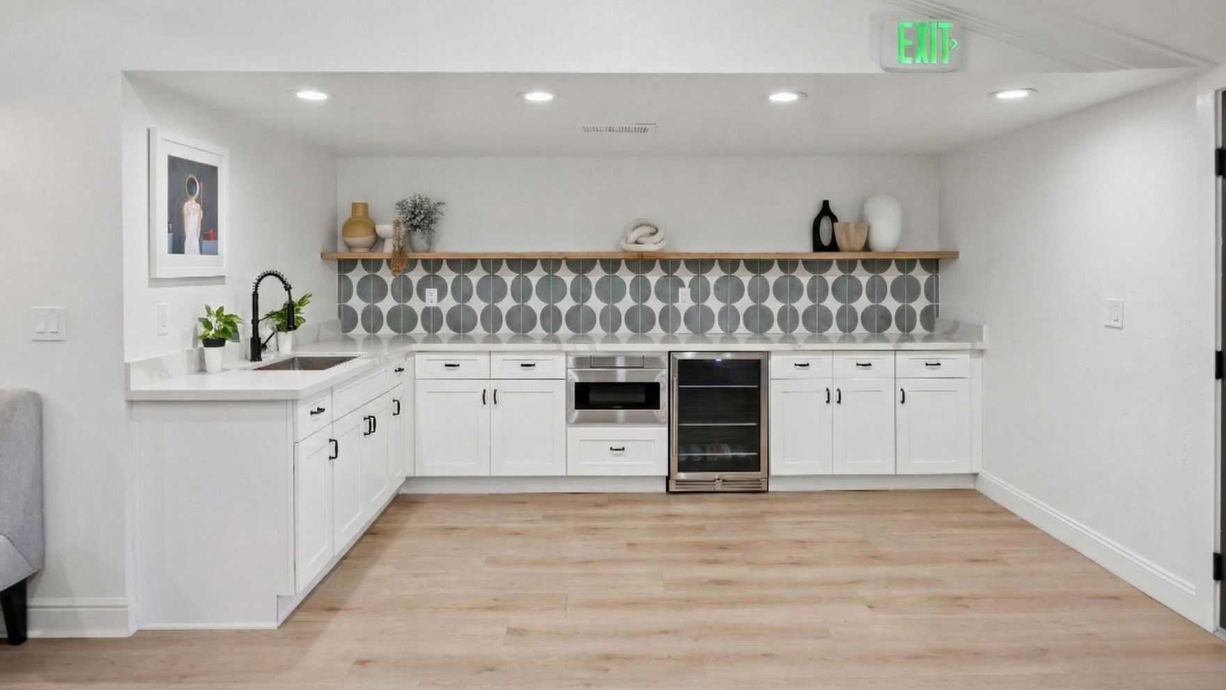 White kitchen with wood floor, black faucet, patterned backsplash, and built-in appliances.