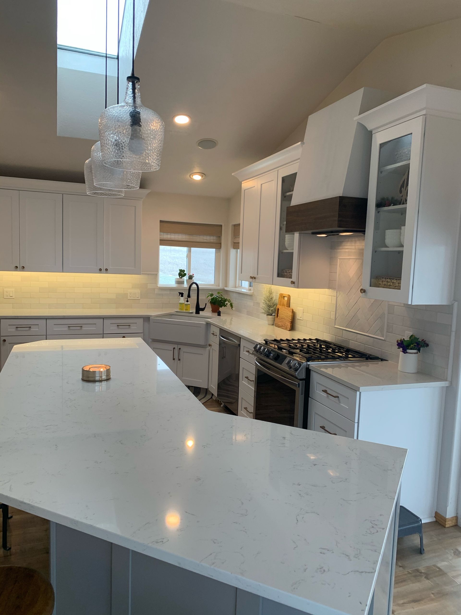 Bright, white kitchen with island and skylight. Stainless steel appliances, white cabinets, and gray countertops.